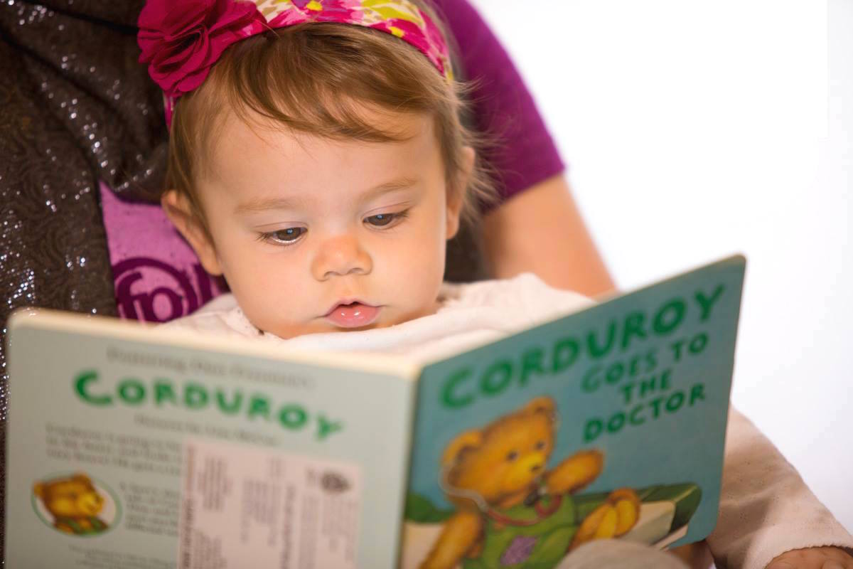A baby looking down at an open Corduroy book.